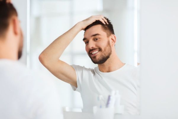 Hombre mirándose al espejo viéndose el trasplante capilar y sus beneficios
