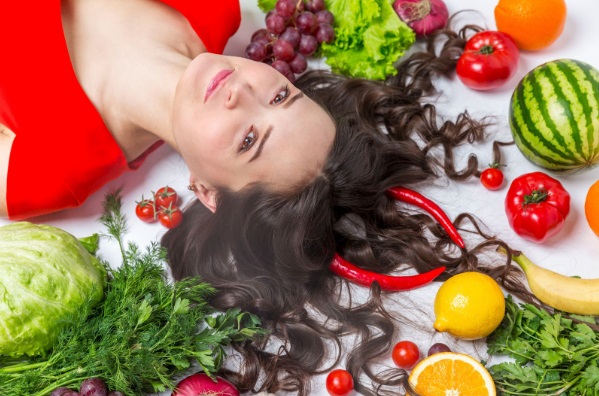 Mujer con un pelo sano rodeada de comida saludable representando que un buen hábito alimenticio favorece la salud capilar