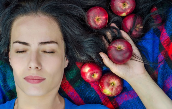 Mujer con pelo sano rodeada de manzanas representando la alimentación sana y la salud capilar