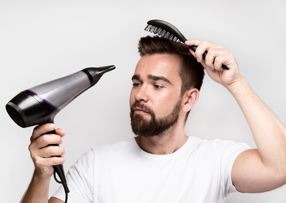 Hombre secándose el pelo con un secador de mano y un peine en la otra