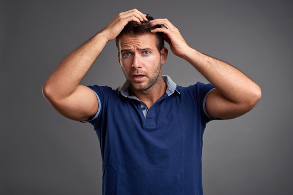 Hombre tocándose el pelo con ambas manos pensando cómo prevenir al caída de su cabello