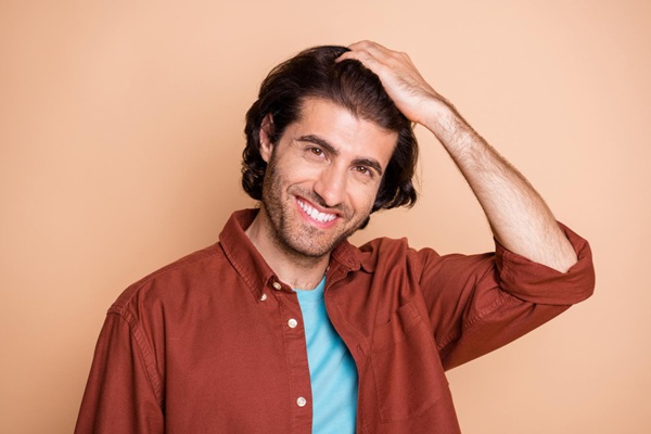 Hombre feliz tocándose el pelo largo representando los tips para hacer crecer el pelo