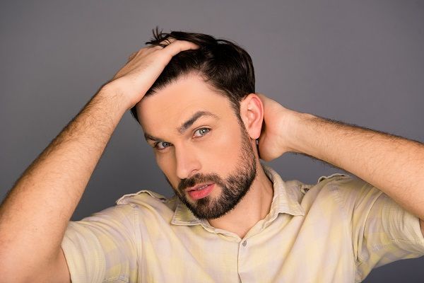 Hombre con barba con las manos puestas en su pelo como si se estuviera peinando